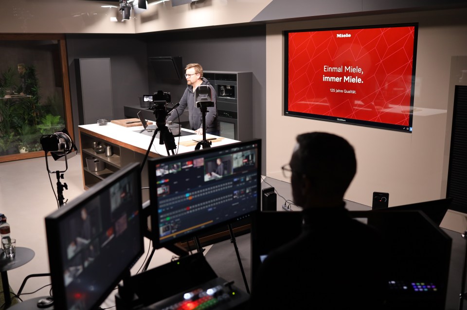 A presenter takes his position behind the Miele-branded kitchen island, surrounded by Canon cameras